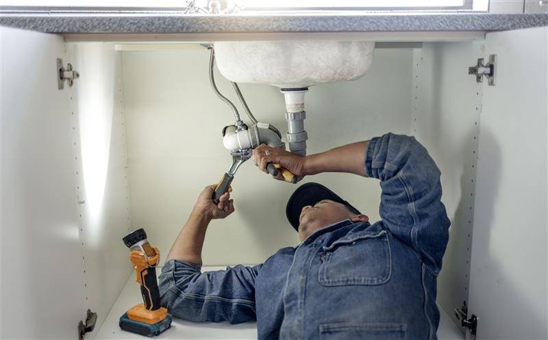 Plumber repairing pipes beneath a bathroom sink in Walnut
